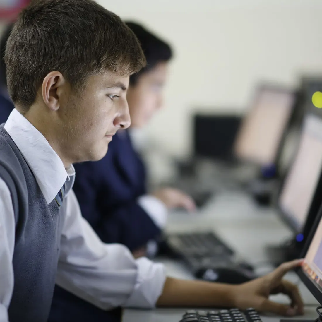 A student in school uniform working at a desktop computer in the IT lab